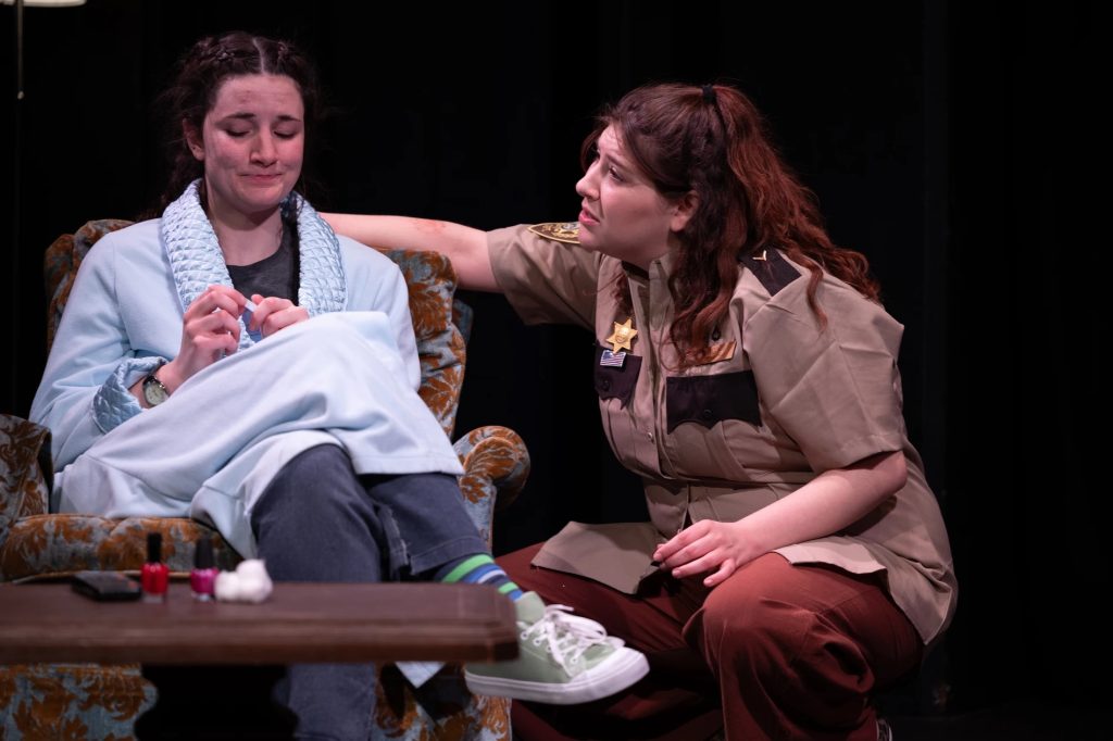 An actor dressed as a police officer talking to an actor in a chair wearing a bathrobe.